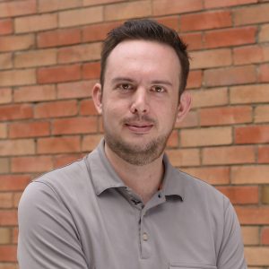 Nolan, Sales Manager for Toronto IT support company Inderly, in grey shirt against brick wall