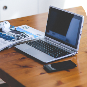 Laptop and phone next to a stack of magazines